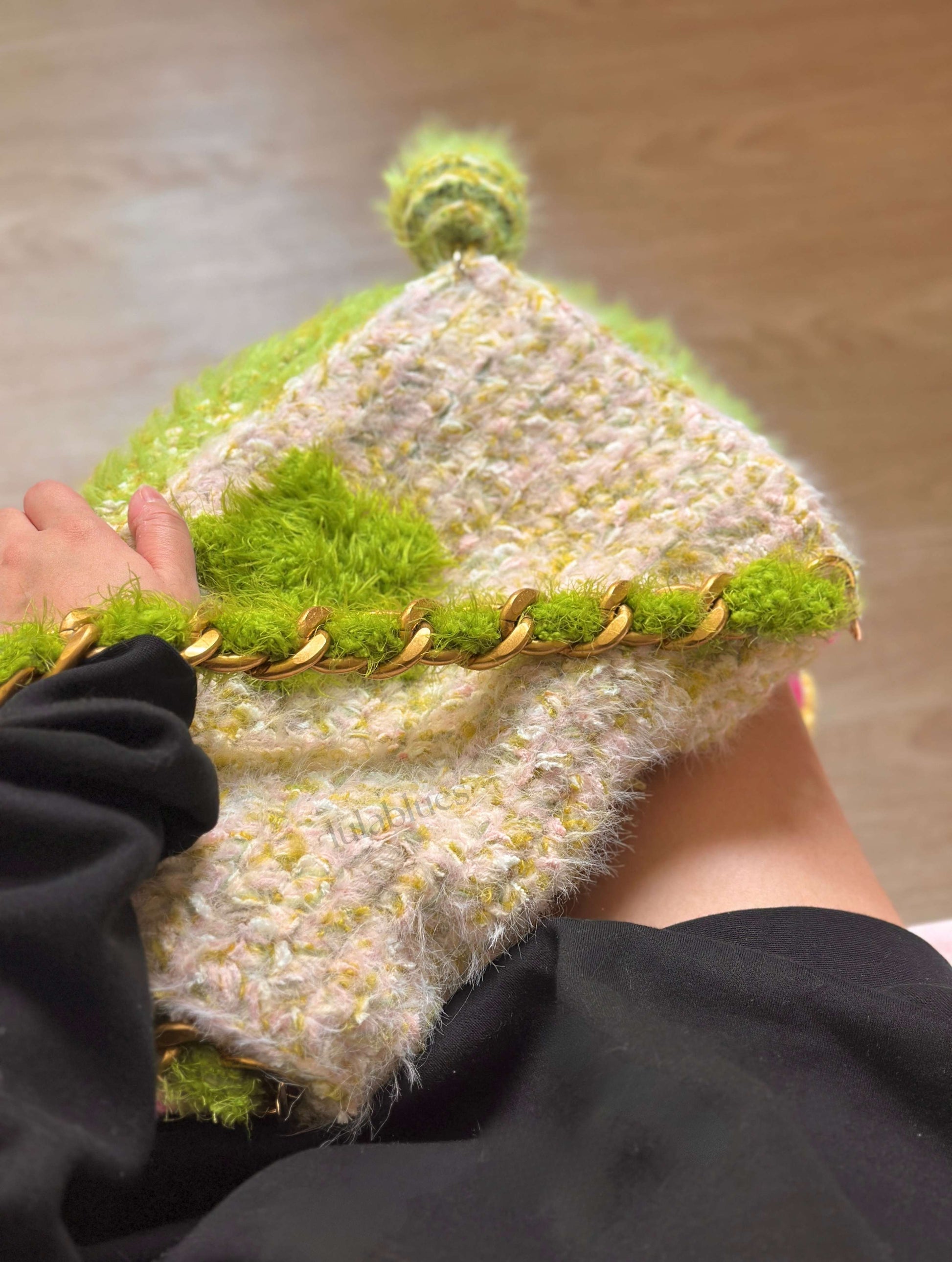 Textured knitted hat with green and beige pattern held by a person.