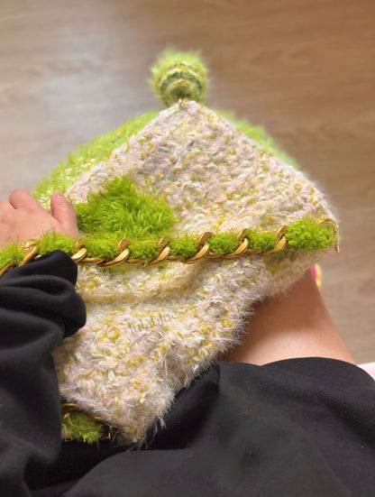 Textured knitted hat with green and beige pattern held by a person.