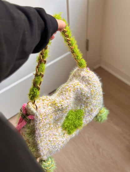 Handbag decorated with flowers and moss held by a person indoors.