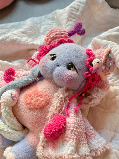 Cute plush toy with pink and purple accents on a soft fabric background