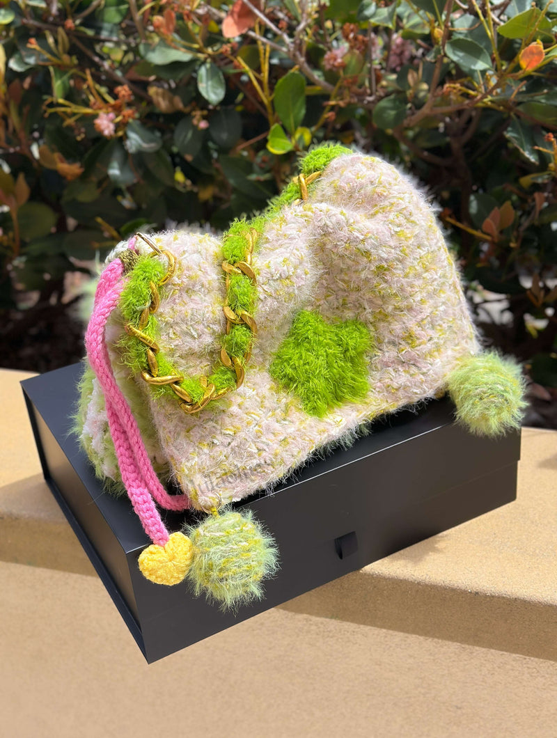 Textured bag with colorful pom-poms on a black stand against a natural background