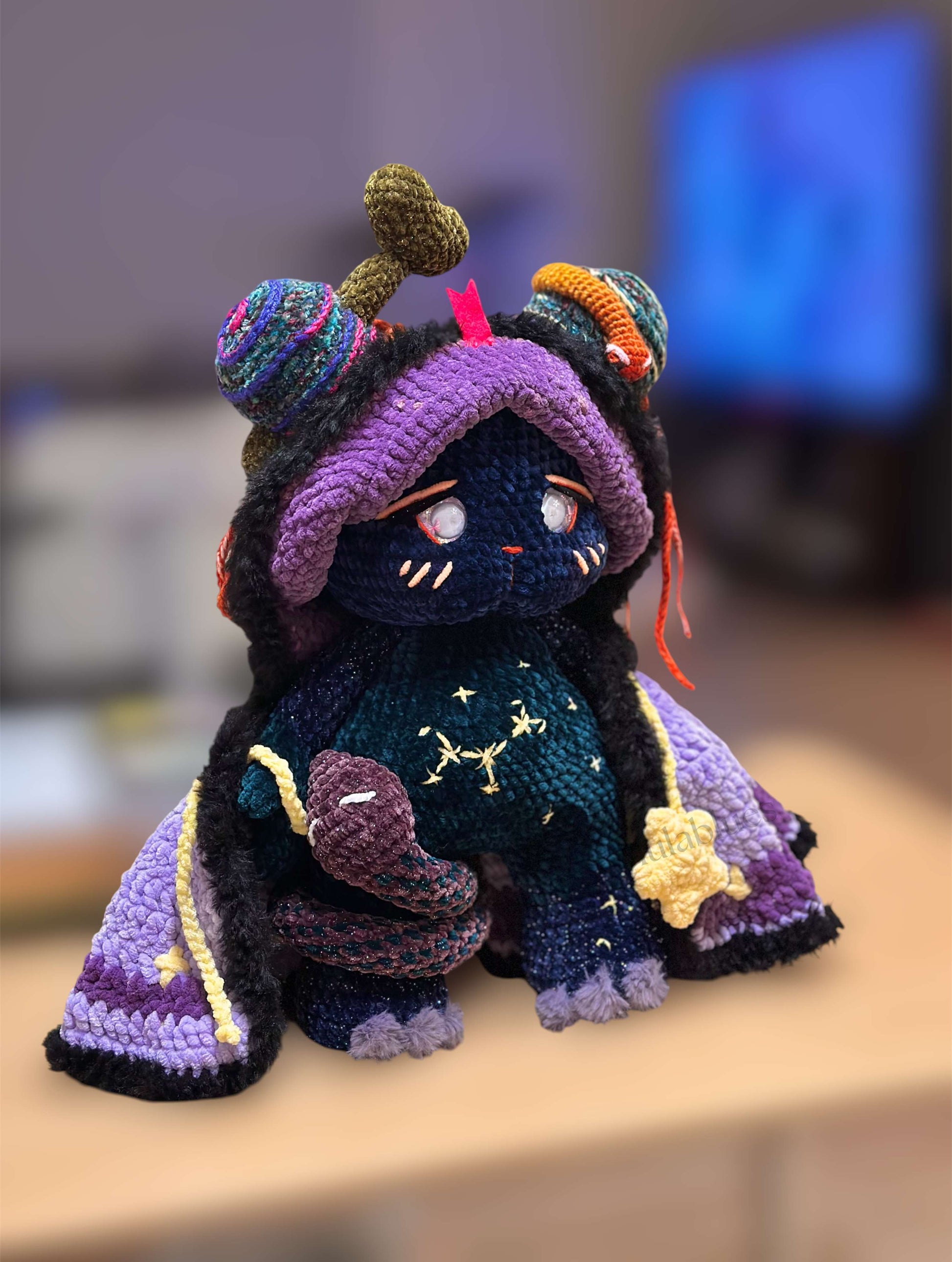 Colorful crochet character with a purple hood and star patterns on a blurred background