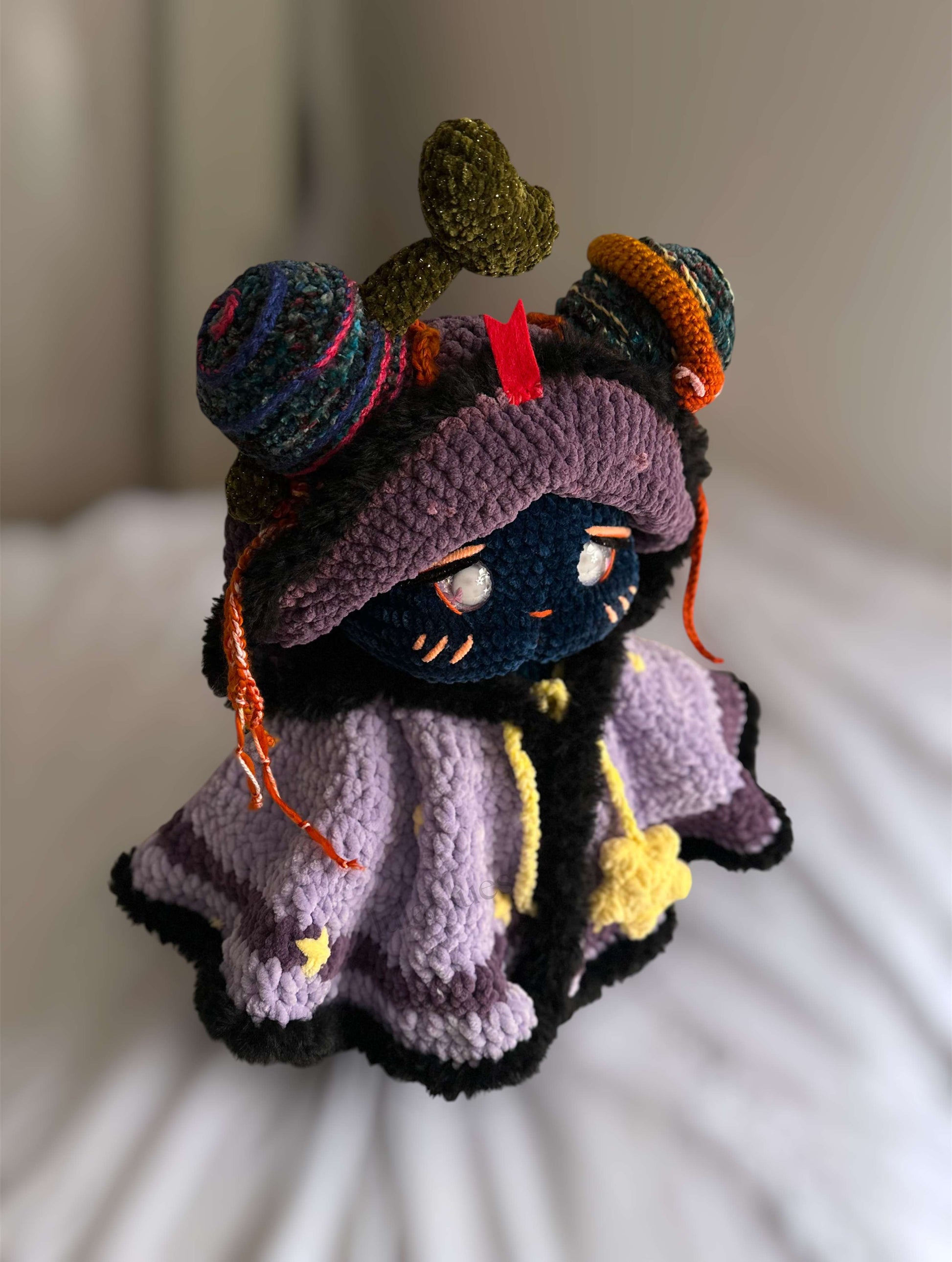 Colorful crochet doll with a purple hat and dress on a white surface